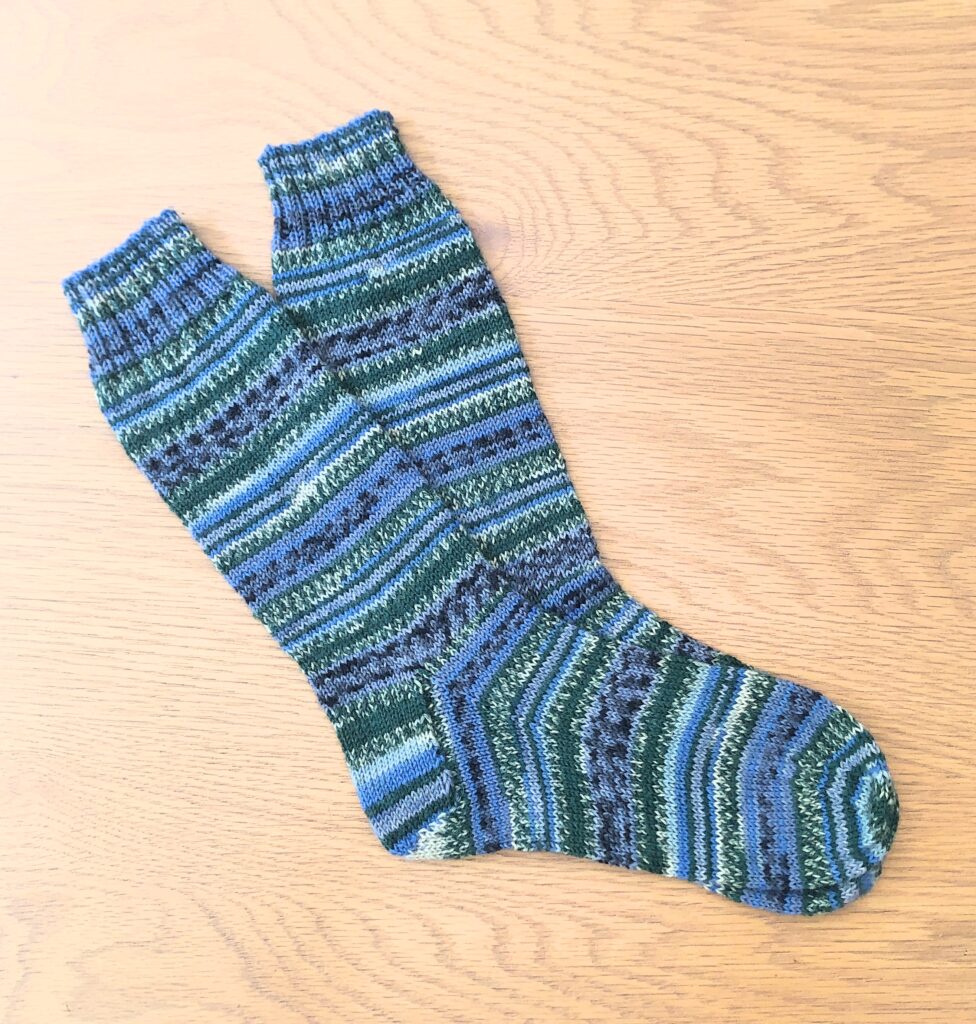 A pair of socks on a wooden table knitted in Arne & Carlos Winter Night Yarn