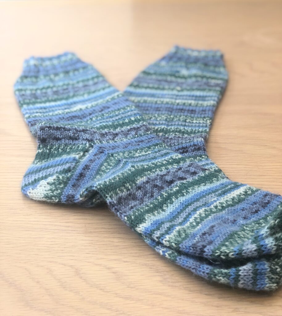 A pair of socks on a wooden table knitted in Arne & Carlos Winter Night Yarn